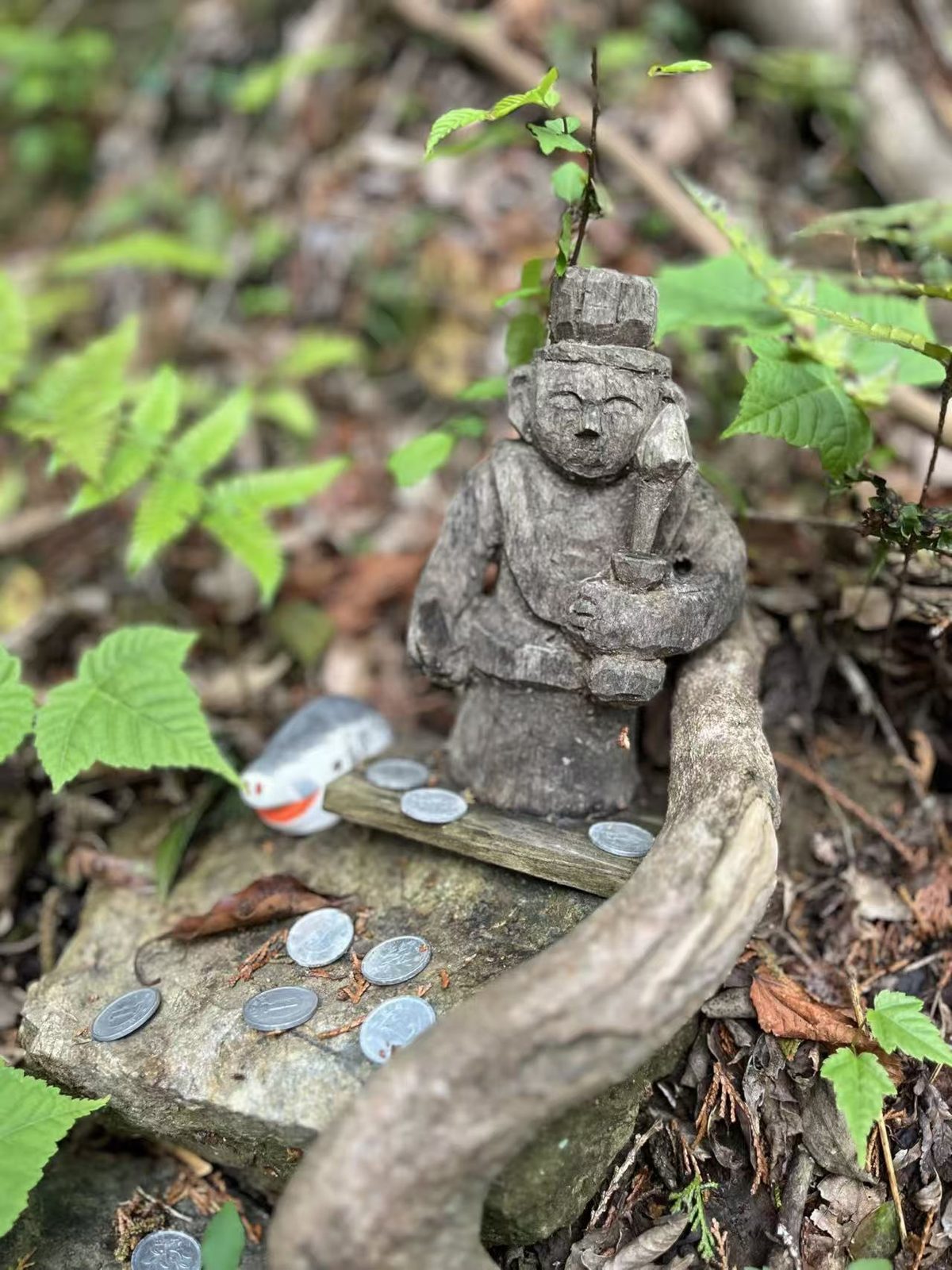 日本山间小径旁的木雕山神像，前方石台上摆着香客供奉的硬币