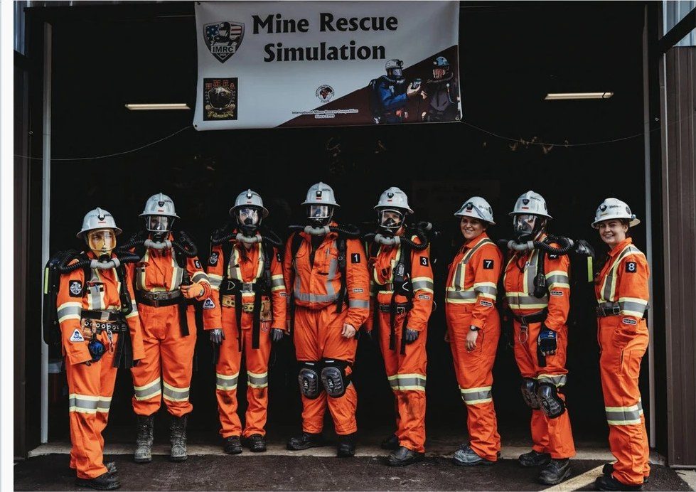 璞玉全女子救援队身穿橙色救援服，站在写着 Mine Rescue Simulation 的横幅下